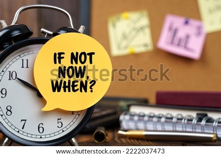 Business concept. The alarm clocks have a sticker with the inscription - If Not Now, When. There are office items in the background in a blurry background.