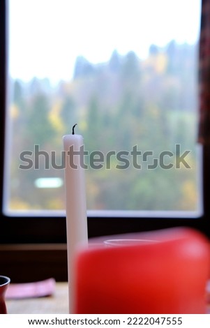 A candle on the background of a window, through the glass of which you can see the autumn forest in the mountains. Vertical picture for social networks