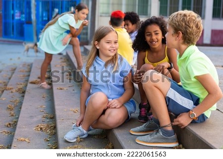 Children talking together while sitting on stairs outdoors. Youngsters chatting during summer day. Royalty-Free Stock Photo #2222061563