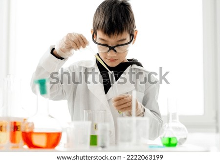 School boy wearing protection glasses doing chemistry experiment in elementary science class. Clever pupil with tubes measuring liquids in laboratory classroom