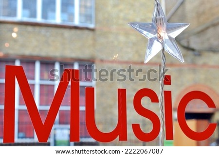 Sticker on a records shop window saying in red capital letters "Music" with a star garland, and a building in the background