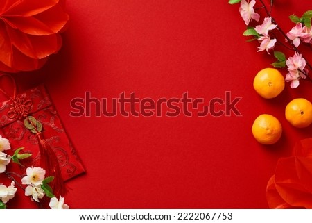 Chinese New Year background with red packet, festival decorations, mandarins, flowers on red table top view. Flat lay.