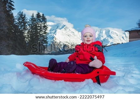 Close portrait of a little smiling girl sit on the sledge in show over mountains going downhill