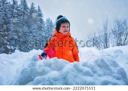 Winter fun: happy boy play outside and throw snow with shovel during Christmas vacations at the mountains