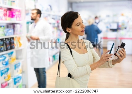 Woman photographing skin or hair care product with smartphone while standing in drugstore.