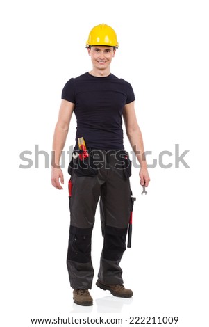 Manual worker in yellow helmet posing and holding wrench. Full length studio shot isolated on white.