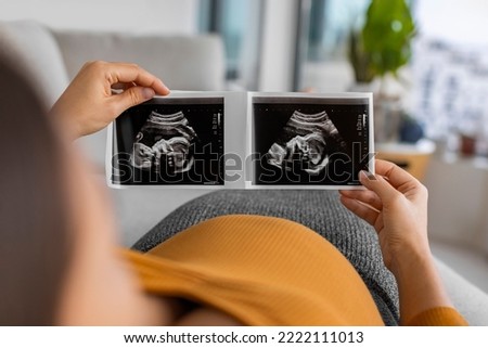 Pregnant woman looking at first ultrasound photo of her baby, caressing her belly happily awaiting the birth of her child. First trimester pregnancy Royalty-Free Stock Photo #2222111013