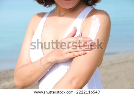 A woman is applying sunscreen and skin care to protect her skin from UV rays. She was applying sunscreen to her shoulders and arms. sunny background Health and skin care concept Royalty-Free Stock Photo #2222116549