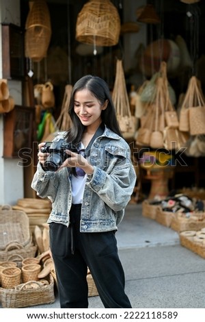 Young cheerful tourist looking at her camera after taking a photo while traveling in the market