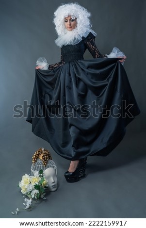 A beautiful girl in a vintage black dress, a white frill and a lush curly wig poses in the studio. Carnival costume.