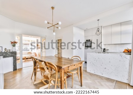 Interior of spacious light dining room with elegant chandelier located near kitchen with comfortable furniture and appliances