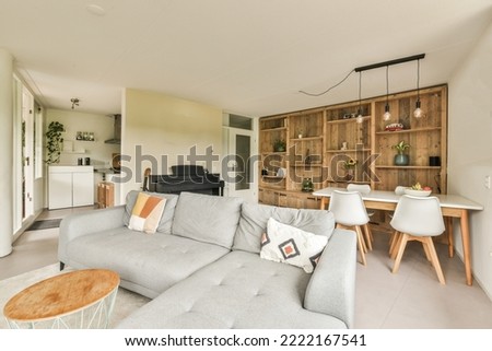 Table with chairs and flowers located near lounge area and kitchen in spacious room of contemporary apartment