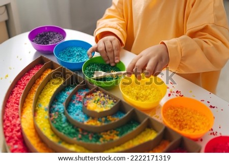 Child hands playing colored rice and make rainbow. Child filled the rainbow with bright rice. Montessori material. Sensory play and learning colors activity for kids.  Royalty-Free Stock Photo #2222171319