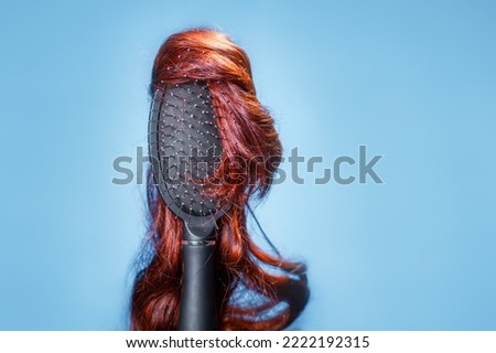 Hair coloring and dye. Comb with red wig on blue background, like woman's head. Hairstyle and beauty salon. Copy space. Concept of hair care, baldness and hairpiece. Royalty-Free Stock Photo #2222192315