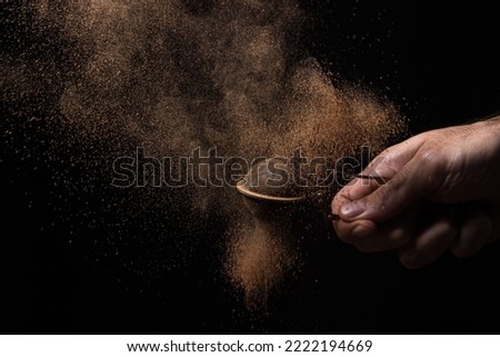 A creative photo of cocoa powder on a black background. Hand with cocoa powder through a small sieve. 
