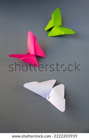 Green, pink and white paper butterfly origami isolated on a blank grey background.
