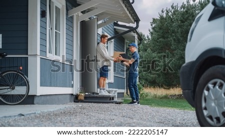 Handsome Young Homeowner Receiving an Awaited Parcel from a Cheerful Courier. Postal Service Worker Comes to the House to Make a Door to Door Delivery and Get a POD Signature on Tablet. Royalty-Free Stock Photo #2222205147
