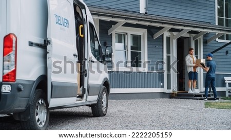 Handsome Young Homeowner Receiving an Awaited Parcel from a Cheerful Courier. Postal Service Worker Comes to the House to Make a Door to Door Delivery and Get a POD Signature on Tablet. Royalty-Free Stock Photo #2222205159