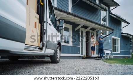 Handsome Young Homeowner Receiving an Awaited Parcel from a Cheerful Courier. Postal Service Worker Comes to the House to Make a Door to Door Delivery and Get a POD Signature on Tablet. Royalty-Free Stock Photo #2222205163