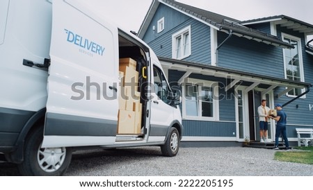 Handsome Young Homeowner Receiving an Awaited Parcel from a Cheerful Courier. Postal Service Worker Comes to the House to Make a Door to Door Delivery and Get a POD Signature on Tablet. Royalty-Free Stock Photo #2222205195