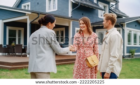 Happy Couple Shaking Hands with Realtor in Front of Their New Home. Professional Real Estate Agent Congratulating Young Homeowners with Property Purchase, Giving Them the Key to the House. Royalty-Free Stock Photo #2222205225
