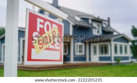 Close Up of a House Sold Sign on a Lawn in Front of a Big Modern House with Traditional Architecture. Housing Market Concept with Residential Property in the Countryside.