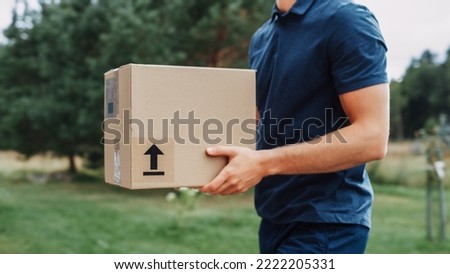 Young Man Working in Delivery Services. Mailman Bringing Cardboard Box From a Delivery Vehicle and Taking the Box to the Homeowner. Courier at Work.