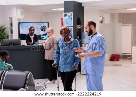 Hospital administrative staff guiding african american patient with degenerative disease to therapist office. Afro female receptionist at sanatorium supporting elderly woman. Royalty-Free Stock Photo #2222224219