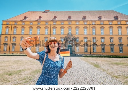 Travel blogger takes selfie photos with german flag on the camera of smartphone of the Osnabruck university campus in old town, Germany