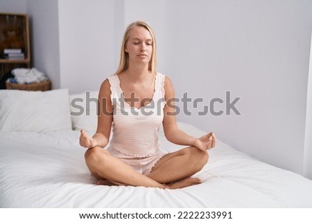 Young blonde woman doing yoga exercise sitting on bed at bedroom