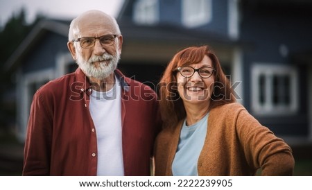 Happy Senior Couple Posing Outdoors Their Residential Area Home, Embracing Each Other. Loving Adults Look at the Camera and Smile, Enjoy Their Carefree Retirement Life.
