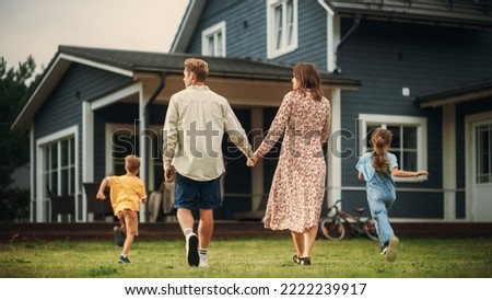Young Beautiful Couple Walking Outdoors Towards the Country House, Holding Hands. Their Little Son and Daughter Running Together with Them. Young Modern Family at Home, Footage from The Back. Royalty-Free Stock Photo #2222239917
