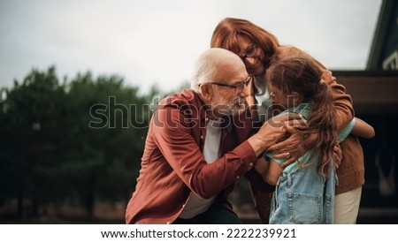 Grandfather and Grandmother are Happy to Meet Their Granddaughter in Front of their Suburbs House. Grandparents Hugging the Girl, Enjoying Family Time with Grandchild. Royalty-Free Stock Photo #2222239921