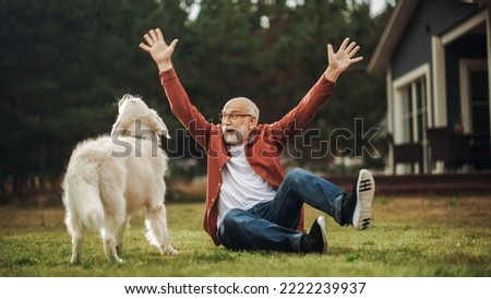 Cheerful Senior Man Enjoying Time Outside with a Pet Dog, Petting a Playful White Golden Retriever. Happy Adult Man Enjoying Leisure Time on a Front Yard in Front of the House. Royalty-Free Stock Photo #2222239937
