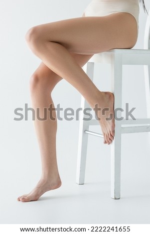 Cropped view of woman in panties sitting on chair on grey background