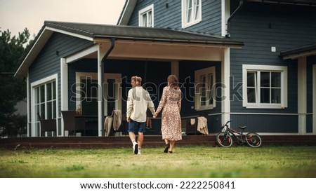 Young Beautiful Couple Walking Outdoors Towards the Country House, Holding Hands. Young Modern Family at Home, Footage from The Back. Royalty-Free Stock Photo #2222250841