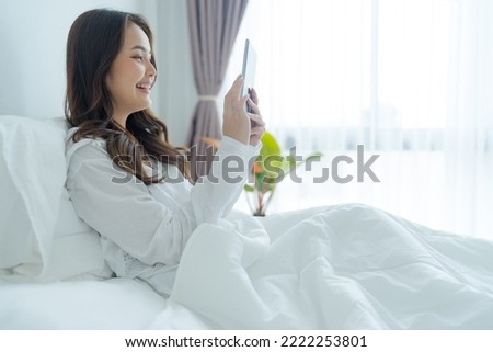 Girl lying in bed playing tablet computer in bedroom with a smiling face, bright, happy, with a relaxed expression