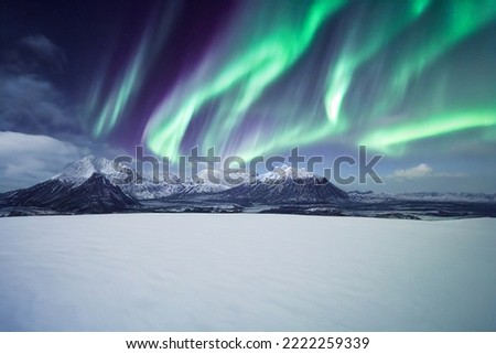 Northern Lights over snowy mountains. Aurora borealis with starry in the night sky. Fantastic Winter Epic Magical Landscape of snowy Mountains.  