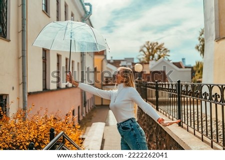 A blonde girl with an umbrella walks around the city against the background of autumn leaves on an autumn day.