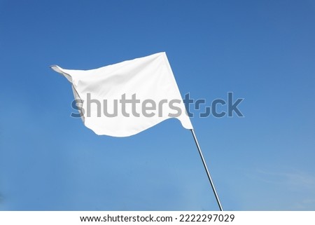 White flag fluttering against blue sky on sunny day Royalty-Free Stock Photo #2222297029