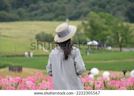 View from behind of a female photographer standing among flower field viewing scenery outdoor. 