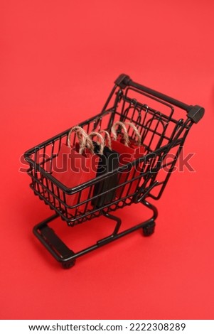 Black shopping cart with paper bags on red background, vertical photo,copy space. black friday concept