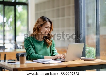 An Asian female accountant sits at a desk with a laptop working and calculates a financial graph showing results about successful investment planning.