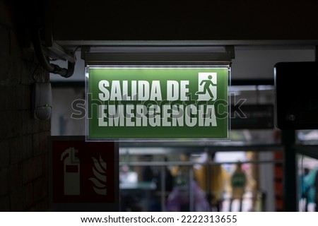 Lit up sign in Spanish emergency exit next to an open door. Safety, danger, natural disaster concept.