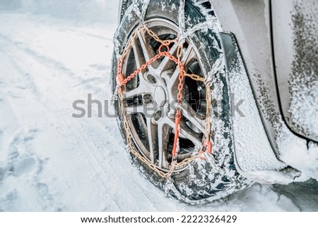 Snow chains on tire. Car wheel with traction chains on a snowy winter road Royalty-Free Stock Photo #2222326429