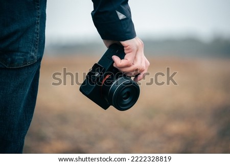 Person in blue jean holding a digital camera in one hand. Blurry background. Autumn