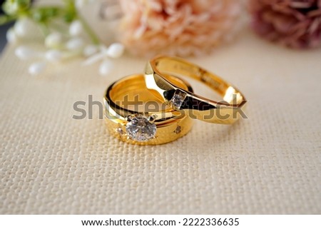 Couple gold wedding rings on a burlap cloth with brown flowers and cream on the back Royalty-Free Stock Photo #2222336635