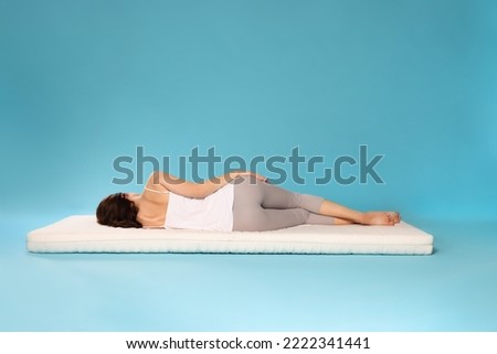 Young woman sleeping on soft mattress against light blue background, back view Royalty-Free Stock Photo #2222341441
