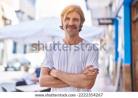 Young blond man standing with arms crossed gesture at street