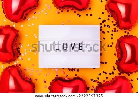 Word Love. Lightbox, confetti and red inflatable foil balloons in a heart shape on a yellow background.